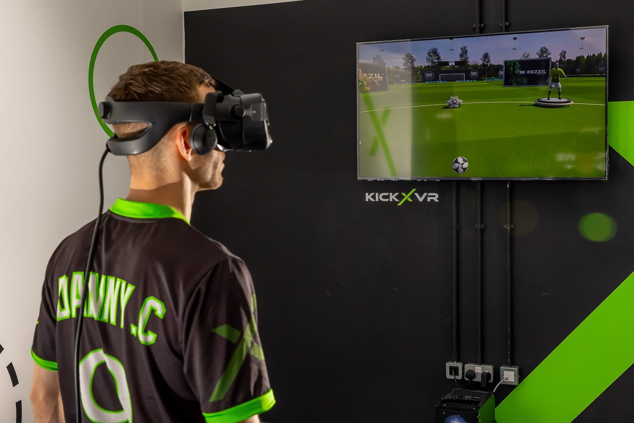 Man wearing a VR football headset and KickX arena ready to play virtual reality football with a tv screen in front of him